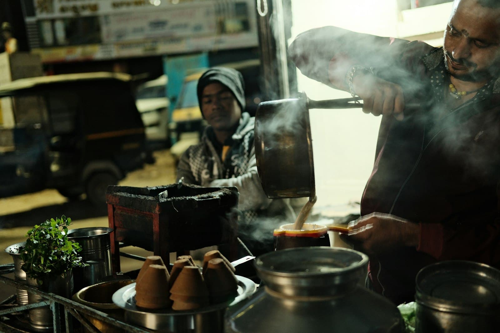 A chai vendor pours steaming tea at a night stall, clay kulhads stacked in front